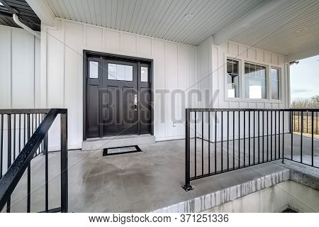Home Entrance With Front Porch And Black Front Door Against White Panelled Wall