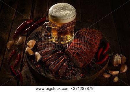 Beef jerky, bresaola, dried beef - Basturma in Red Pepper with black pepper peas, chilli,  garlic and wit pint of beer on a dark wooden background. Armenian national snack 
