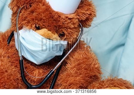Portrait Of Tired Teddy Bear Doctor With Protective Medical Mask And Stethoscope. Teddy Bear Sits Wi