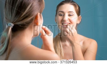 Young Woman Cleaning And Checking Her Teeth At Mirror In Bathroom