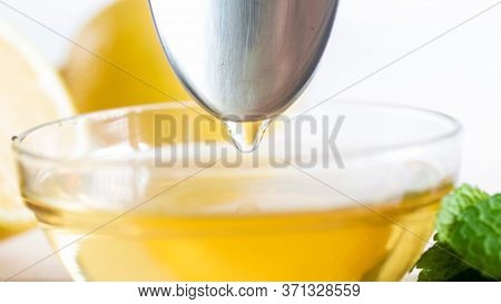 Closeup Image Of Honey Dropelts Falling From Metal Spoon In Honey Jar