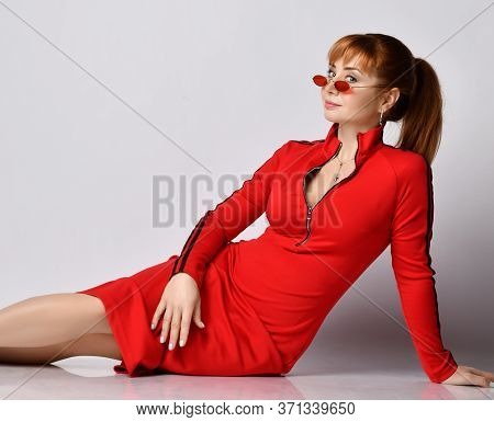 Portrait Of Young Beautiful Smiling Red-haired Woman In Casual Red Dress And Sunglasses Sitting On F