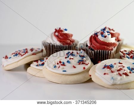 Pile Of Sugar Cookies With White Frosting And Red White And Blue Sprinkles With Mini Chocolate Cupca