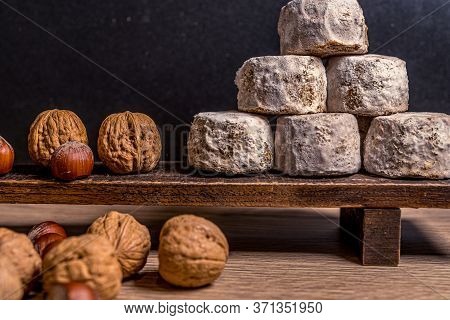French Cheese Crottin De Chavignol In The Dark Background. Composition With Hazelnuts And Walnuts. H