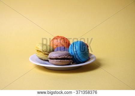 Macaroons Of Differrent Colours On A Saucer Isolated On Yellow Background. Image Contains Copy Space