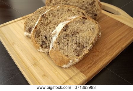 Sliced Walnuts Bread On Wooden Cutting Board On Dark Brown Background. Fresh Brown Bread With Walnut