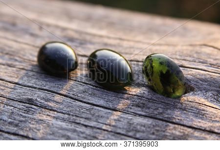 Black Jade Translucent Green Stone In Sunlight On Wood. The Black Jade Is Dark Green In Color, But U