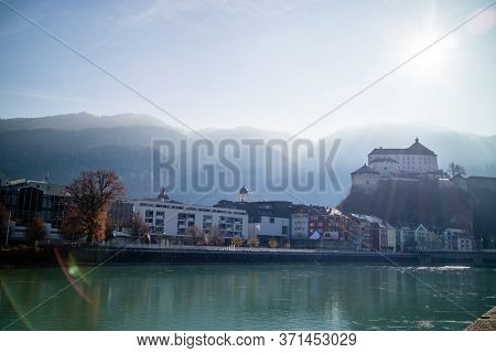 Amazing autumn landscape with Kufstein Fortress and traditional houses on a boardwalk of smooth Inn river on a forefront on a background of clear sunny sky, Kufstein Austria.
