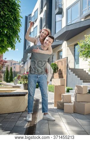 Smiling Woman Sitting On Her Husbands Back And Holding The Key From New House