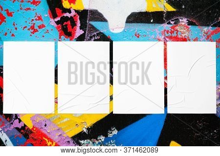 Closeup of colorful messy painted urban wall texture with four wrinkled glued poster templates. Modern mockup for design presentation with clipping path. Creative urban city background.