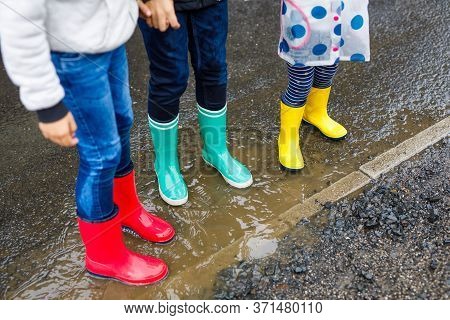 Close-up Of Three Children, Toddler Girl And Two Kids Boys Wearing Red, Yellow And Green Rain Boots 