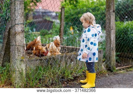 Outdoor Portrait Of Happy Smiling Little Toddler Girl Wearing Rain Jacket On Rainy Cloudy Day Feedin