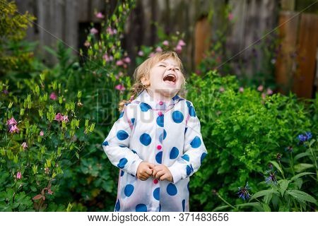Outdoor Portrait Of Happy Smiling Little Toddler Girl Wearing Rain Jacket On Rainy Cloudy Day. Cute 