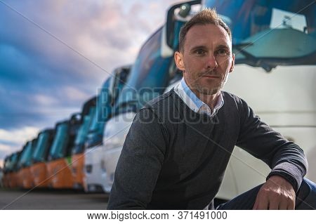 Caucasian Transportation Company Owner In His 40s And His Coach Buses Fleet In Background. Company B