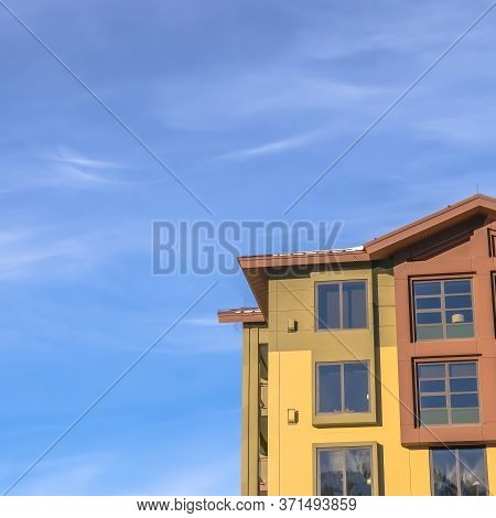 Square Frame Home Exterior With Balconies And Multi Color Walls Against Blue Sky And Clouds