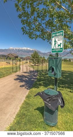 Vertical Crop Pet Waste Station With Dog Poop Bags And Garbage Can Beside A Tree And Pathway