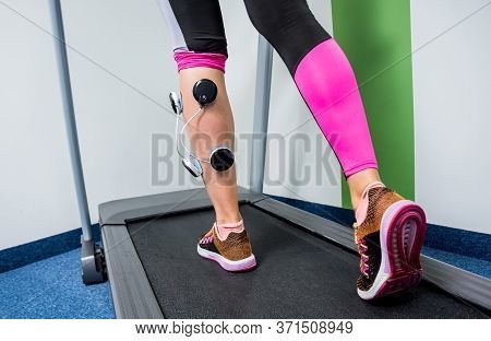 Young Sports Woman With Electrostimulator On The Muscles Of The Legs.