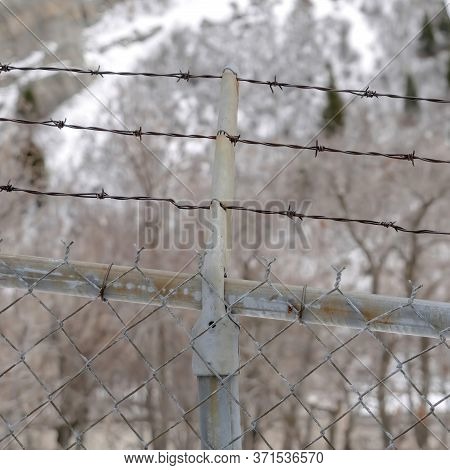 Square Focus On Security Chain Link Fence With Barbed Wires Against On Snowy Hill Slope