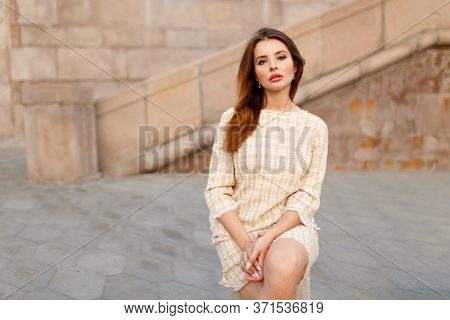 An Unhappy Woman Stays Alone In The City, Sits With Her Legs Crossed, Dressed In A Dress With Straig