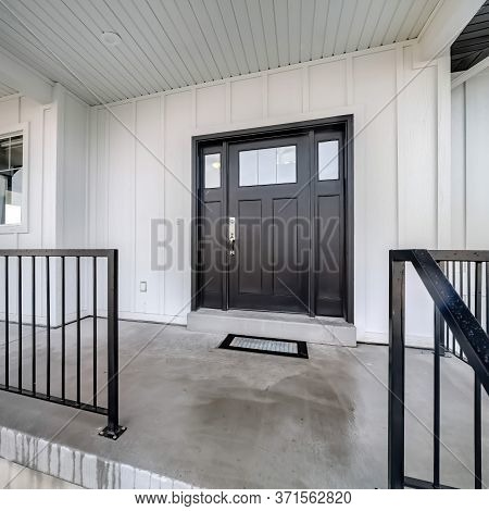 Square Home Entrance With Front Porch And Black Front Door Against White Panelled Wall