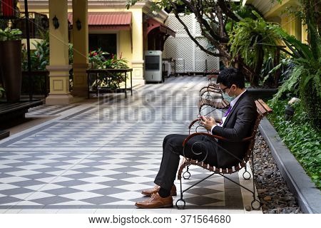 Asian Young Businessman Wearing Hygiene Face Mask And Reading Pandemic News Of Coronavirus Or Covic-