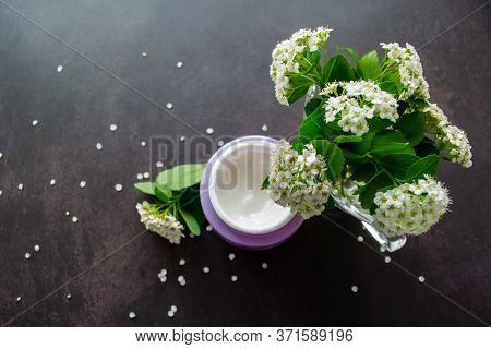 Spirea Twigs With White Flowers And Green Leaves Under Which There Is A Lilac Jar With A White Cream