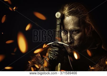 Close-up portrait of a medieval knight in armour and with a sword over black background. Historical reenactment.
