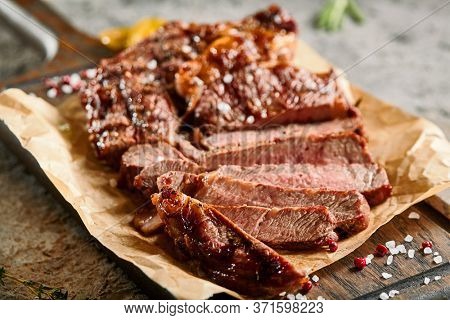 Classic ribeye steak served in waxed paper on wooden cutting board. Cut against grain beef steak. Roasted beef steak with yellow chilli pepper slices and salt crumbs. Rustic spoon and spice bowl
