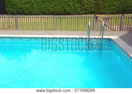 Modern Swimming Pool With Pool Cover For Protection Dirt Rolled Up And Pool Ladder In Garden.
