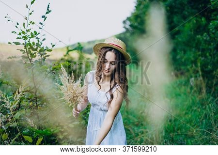 Beautiful Girl In A Board And Hat Collects Flowers. The Girl Collects A Bouquet Of Dried Flowers. Br