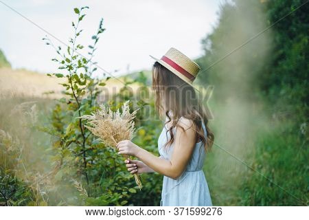 Beautiful Girl In A Board And Hat Collects Flowers. The Girl Collects A Bouquet Of Dried Flowers. Br