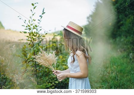 Beautiful Girl In A Board And Hat Collects Flowers. The Girl Collects A Bouquet Of Dried Flowers. Br