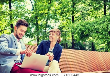 Businessman discussing plans over laptop with beautiful businesswoman while sitting on bench
