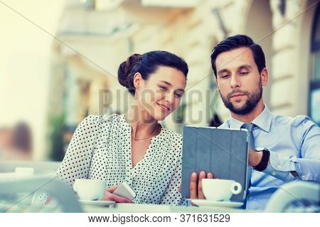 Businessman discussing plans over digital tablet to businesswoman while sitting and waiting for their food at restaurant
