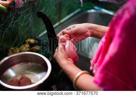 An Indian Woman Cutting Pieces Of Chicken With Boti, A Long Curved Knife Fixed On A Wooden Platform