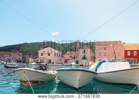 Waterfront View Of Old Simple Boats Docked In The Harbour Of Starigrad, Hvar. City Square In The Bac