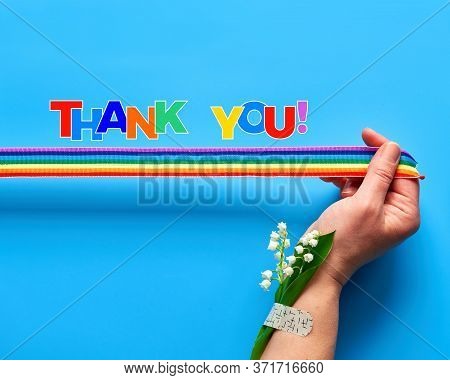 Rainbow Ribbon In Womans Hand. Chamomile Flowers And Grass Bouquet Attached To Wrist With Medical Pa