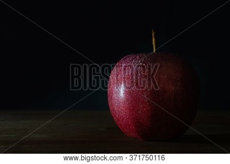 Red Apple With Water Drops On Wooden Surface With A Black Background