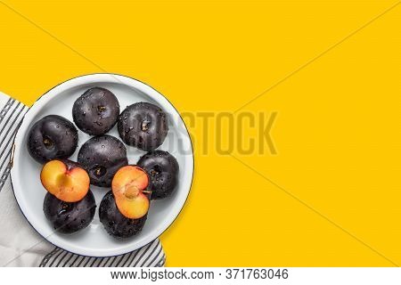 Ripe Juicy Dark Plums Cut In Half On White Plate On Yellow Background. Summer Autumn Fruits Jam Maki