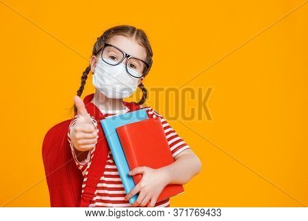 Smart Girl In Mask And Glasses Hugging Textbooks And Shows Tumb Up While Studying At School During P
