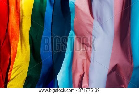 closeup of a gay pride flag and a transgender pride flag waving on the blue sky, moved by the wind