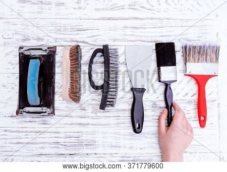 Old Tools (paint Brushes, Spatula, Wire Brush, Sand Paper Holder) And Hand Taking One Brus One On Wh
