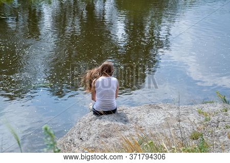 a lonely girl sits on a rock near the river
