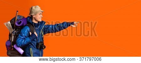 Excited Hicker With Big Backpack Pointing At Free Space Over Orange Studio Background, Panorama