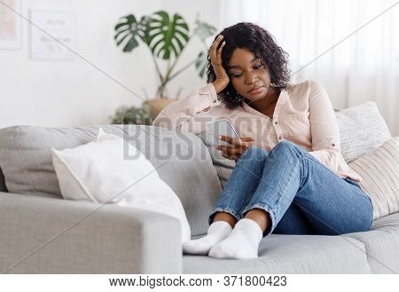 Upset African American Girl Using Smartphone While Sitting On Couch At Home, Having Depression, Wait