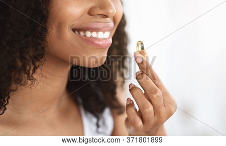 Beauty Supplement. Smiling Black Girl Taking Biotin Vitamin Capsule For Healthy Skin, Cropped Image,