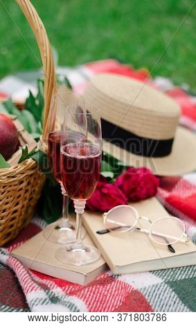 on the grass there is a checkered plaid and on it is a basket with strawberries, peaches, in the gla