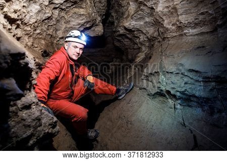 Man Walking And Exploring Dark Cave With Light Headlamp Underground.