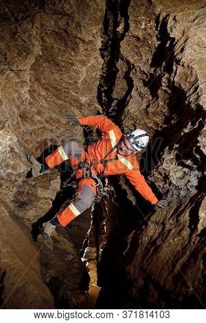Speleologist Descend By The Rope In The Deep Vertical Cave Tunnel.