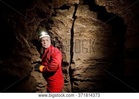 Man Walking And Exploring Dark Cave With Light Headlamp Underground.